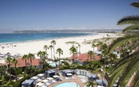 Hotel del Coronado's buildings and pool with the beach and bay of Coronado Island.