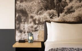 Wall photo art of a person on a mountain bike on Sedona trail with a bed with two pillows and side table with lantern and clock at Mountain Modern Sedona.