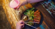 A woman holds a martini glass with a cocktail in it and a man eats sliced steak out of a bowl with chopsticks from CHoP Chandler.