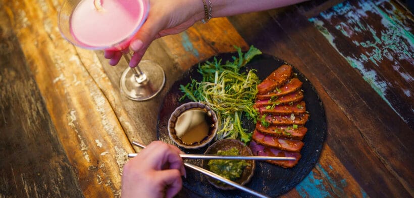 A woman holds a martini glass with a cocktail in it and a man eats sliced steak out of a bowl with chopsticks from CHoP Chandler.