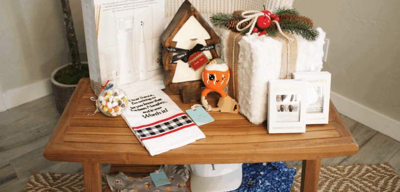 A SmartMouth dental gift set, The Collective, a baby rattle and onsie and other products from Chandler Fashion Center on a table.