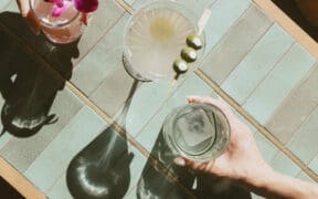 The hands of two people hold cocktails with another cocktail in the middle at Estelle restaurant in Scottsdale