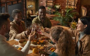 Diverse group of people clinking glasses while enjoying dinner party with friends and family in cozy interior