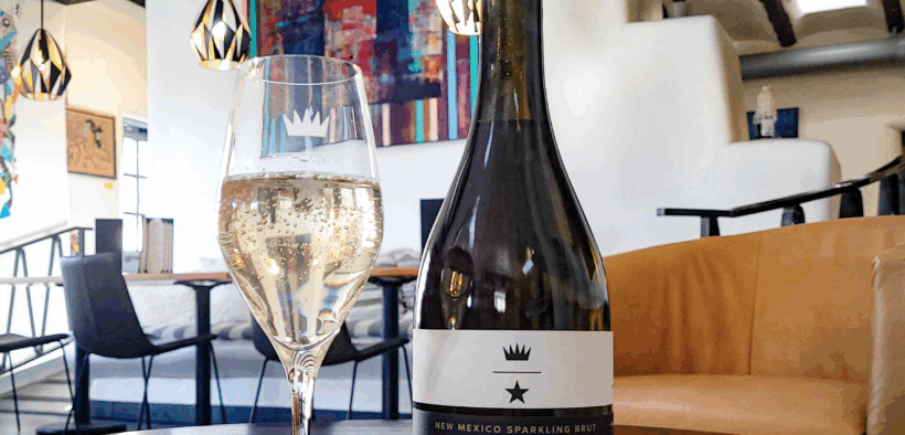 A bottle of Vara wine next to a glass of sparkling wine with the VARA Winery tasting area in the background.