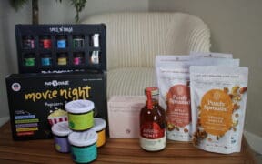 Pop 'n Dulge backyard spices, popcorn gift set, Eveiday chili sauces, a tea sampler set, Holiday Honey and Purely Sprouted snacks on a table.