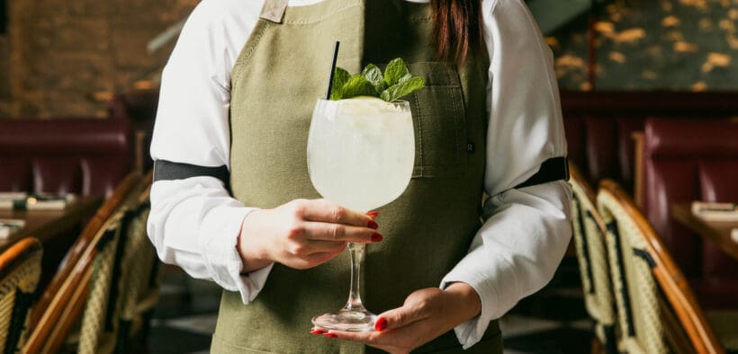 A Pinyon restaurant server holds a large goblet cocktail with mint garnish.