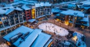 Snowmass winter base village with people on an ice-skating rink that's surrounded by lodging and holiday festivities.