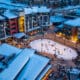 Snowmass winter base village with people on an ice-skating rink that's surrounded by lodging and holiday festivities.