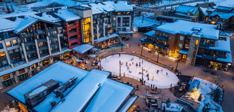 Snowmass winter base village with people on an ice-skating rink that's surrounded by lodging and holiday festivities.