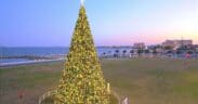 A large lit Christmas tree fenced in with Port Aransas in the back ground in Corpus Christi.