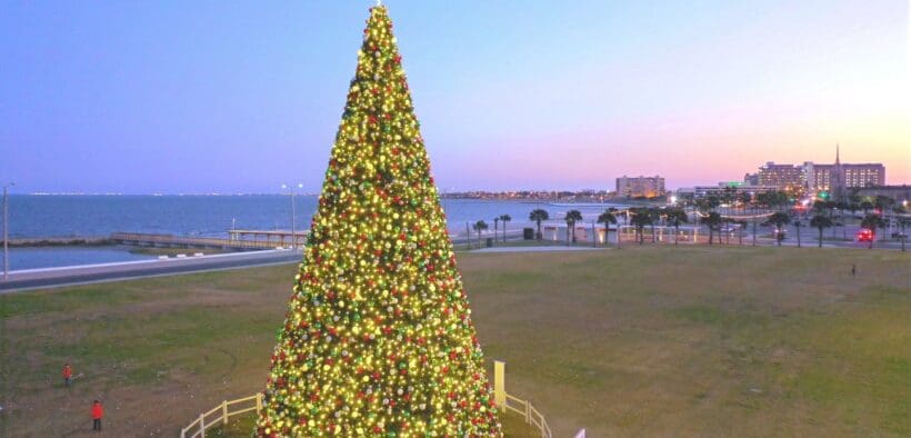 A large lit Christmas tree fenced in with Port Aransas in the back ground in Corpus Christi.