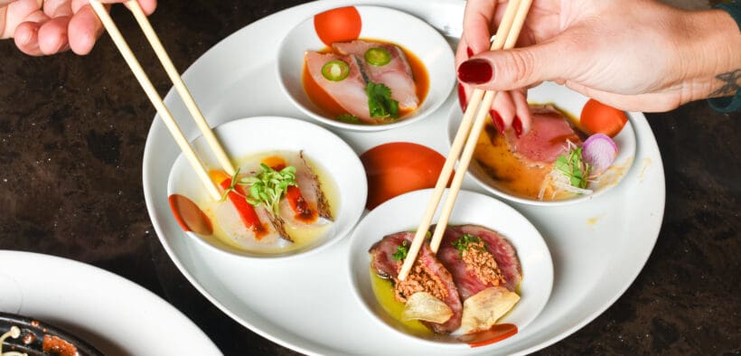 Two hands hold chopsticks, enjoying small bowls of Winter Omakase at Nobu Scottsdale.