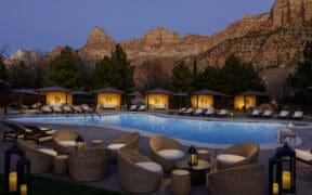 The Red Cliffs Lodge Zion pool and cabanas lit at night against the red cliffs of Zion.