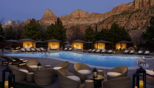 The Red Cliffs Lodge Zion pool and cabanas lit at night against the red cliffs of Zion.