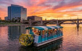 Tempe Town Lake at sunset, with a view of buildings and bridge and the Tempe Boat Cruisin' pedal boat.