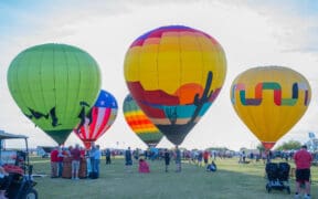 Five hot air balloons with varying designs, mostly with desert depictions at Wild Horse Pass for the Arizona Balloon Classic.