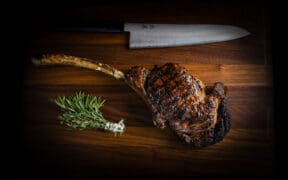 A ribeye and rosemary sprig with a large steak knife on a wood carving platter at BOA Steakhouse.