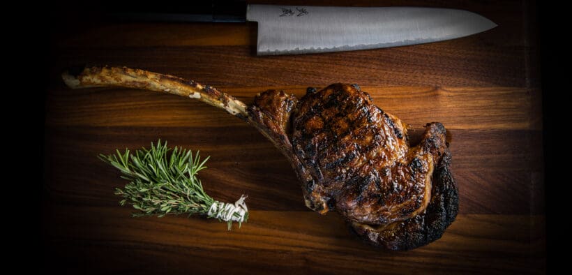 A ribeye and rosemary sprig with a large steak knife on a wood carving platter at BOA Steakhouse.