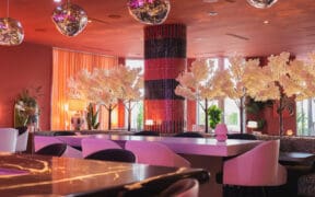 Oversized pink dining chairs surround marble tables with white cherry tree decor at Camello restaurant.
