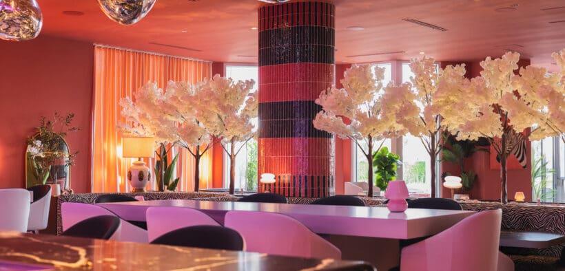 Oversized pink dining chairs surround marble tables with white cherry tree decor at Camello restaurant.