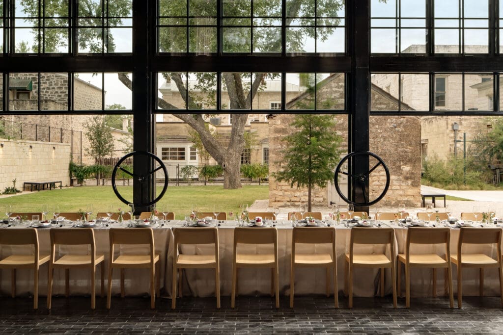 A long community table set for an elevated meal overlooking the lawn and buildings at the Albert Hotel in Texas.