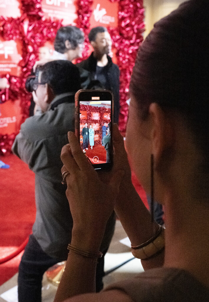 A woman holds her phone up to take a video of celebrities on the red carpet at the Dallas International Film Festival.