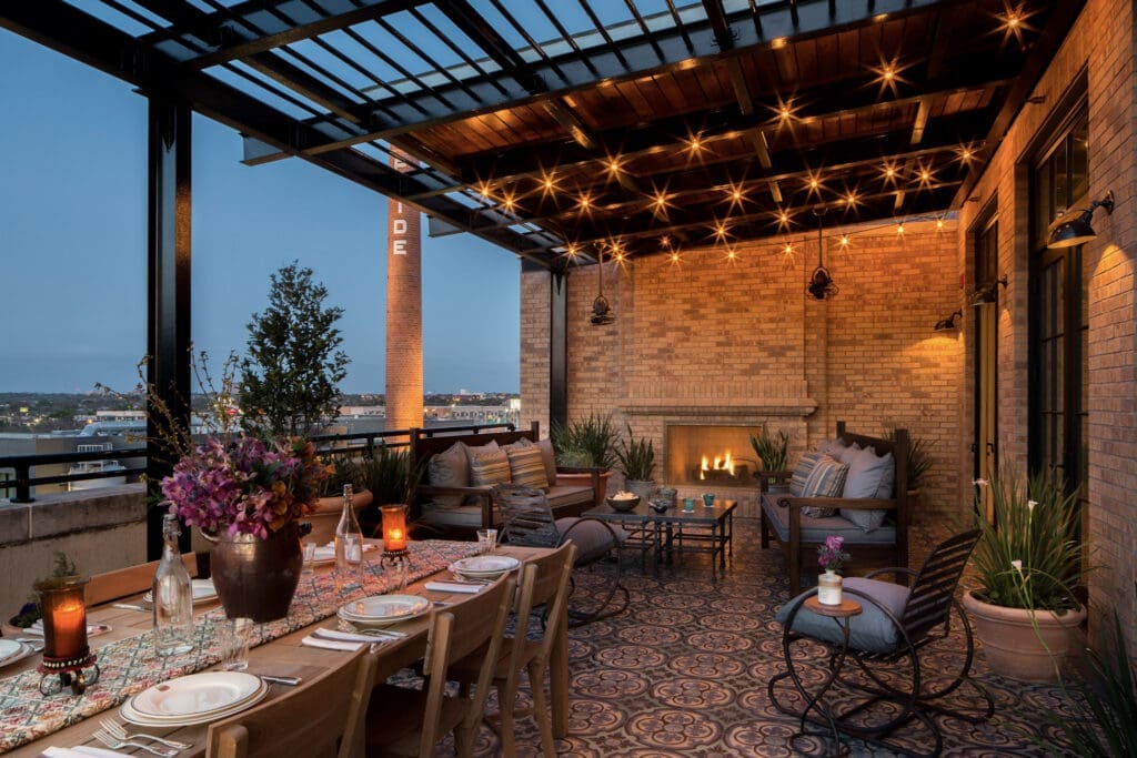 Emma Kohler Suite Terrace at Hotel Emma with a ornate set table overlooking Downtown San Antonio and a lit fireplace.