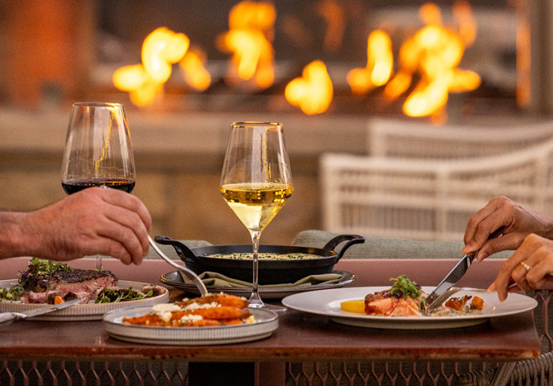 Couple enjoying a romantic candlelit dinner at Laurel Restaurant at Hotel Viata in West Lake Hills, featuring wine, shared plates, and a warm fireside ambiance.