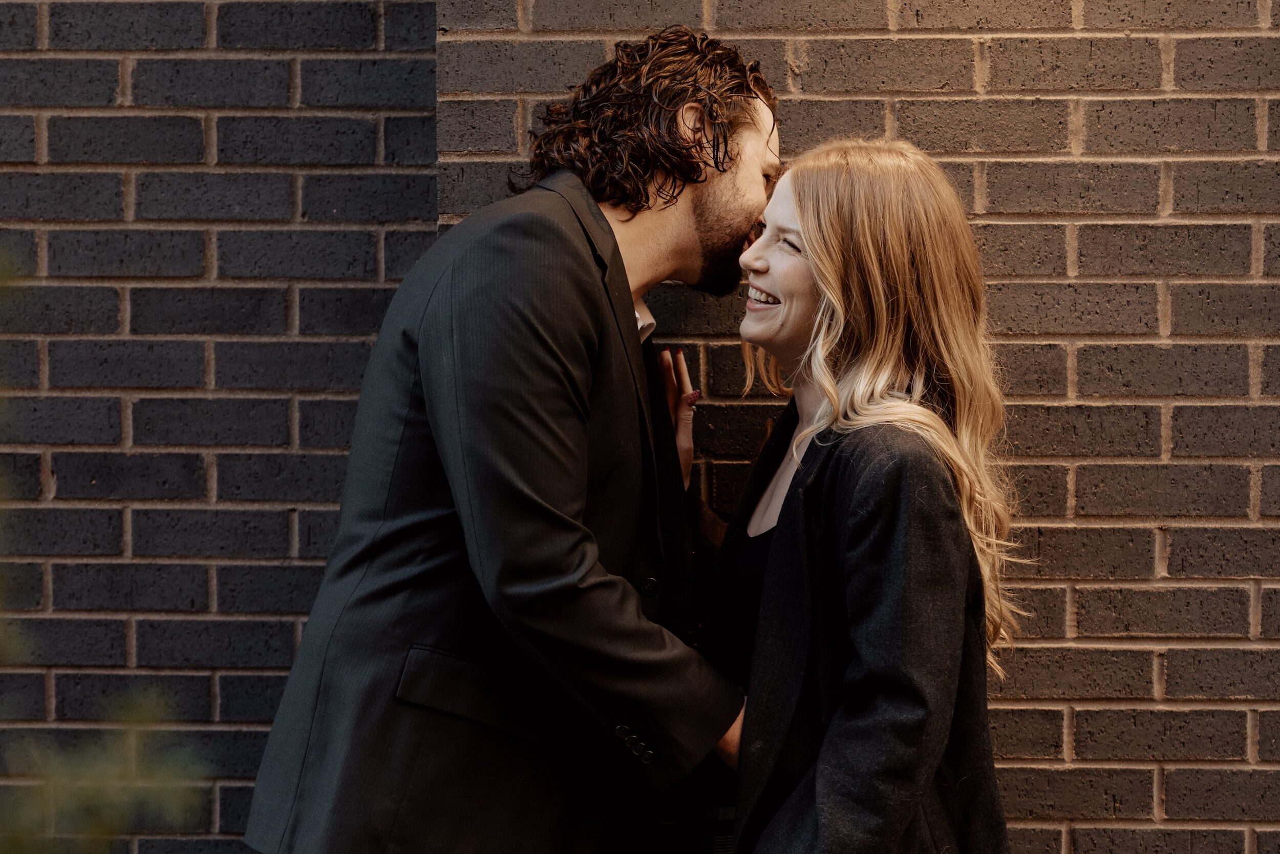 Couple laughing together on a Valentine’s Day date night in front of a brick wall at The Maven Hotel in Downtown Denver.