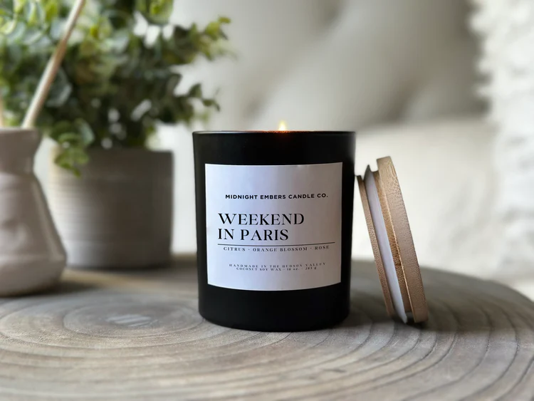 “Weekend in Paris” luxury candle by Midnight Embers Candle Co., featuring a black vessel and wooden lid, softly lit in a cozy home setting.