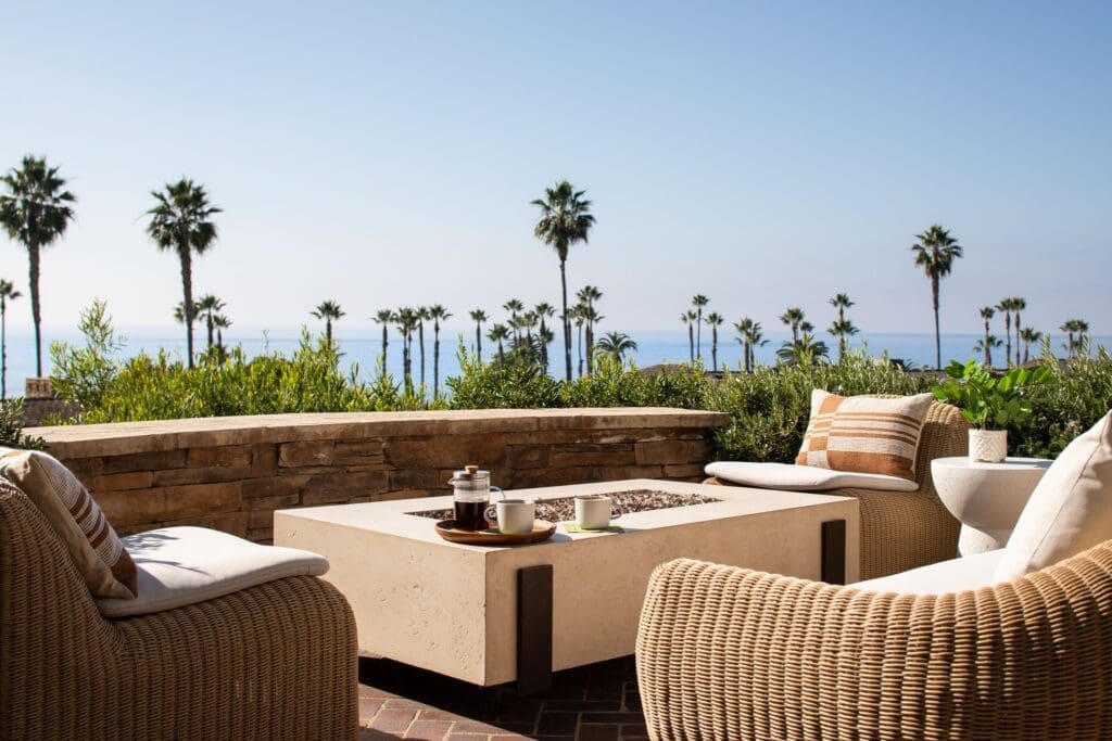 Oceanview outdoor lounge at Montage Laguna Beach with woven seating, fire table, and palm-lined Southern California coastline.