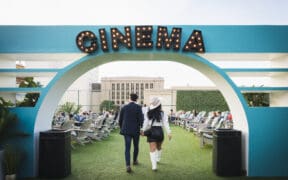 Couple walking hand in hand beneath the Rooftop Cinema Club Fort Worth entrance sign, setting the tone for a romantic Valentine’s Day movie night experience.