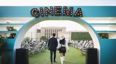 Couple walking hand in hand beneath the Rooftop Cinema Club Fort Worth entrance sign, setting the tone for a romantic Valentine’s Day movie night experience.