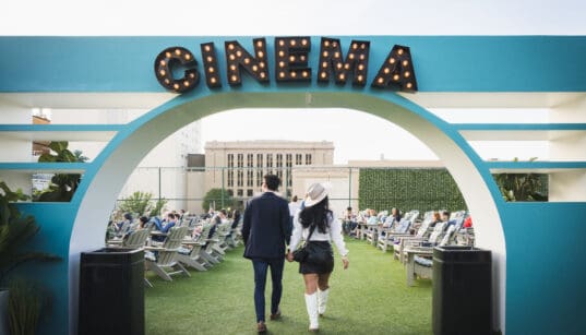 Couple walking hand in hand beneath the Rooftop Cinema Club Fort Worth entrance sign, setting the tone for a romantic Valentine’s Day movie night experience.