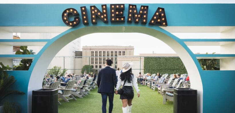 Couple walking hand in hand beneath the Rooftop Cinema Club Fort Worth entrance sign, setting the tone for a romantic Valentine’s Day movie night experience.