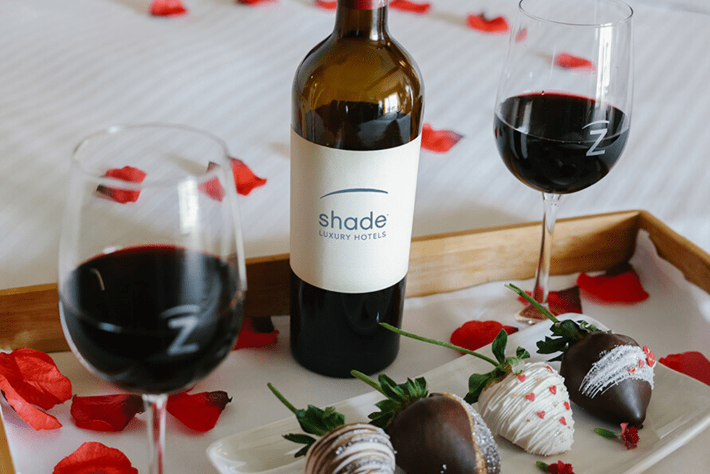 Romantic in-room Valentine’s setup at Shade Manhattan Beach with wine, chocolate-covered strawberries, and rose petal details.