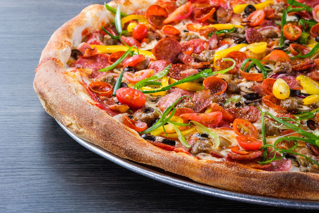 Close-up of a fully topped pizza with pepperoni, sausage, peppers, and tomatoes on a golden-brown crust.
