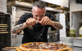 Gemignani sprinkles cheese on a large round pizza at Slice House in Boulder.