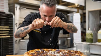 Gemignani sprinkles cheese on a large round pizza at Slice House in Boulder.