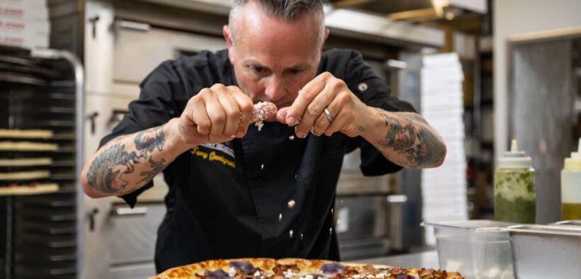 Gemignani sprinkles cheese on a large round pizza at Slice House in Boulder.