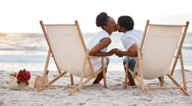 Happy Black couple spending a day at the sea together, kissing from their beach chairs.