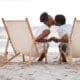 Happy Black couple spending a day at the sea together, kissing from their beach chairs.