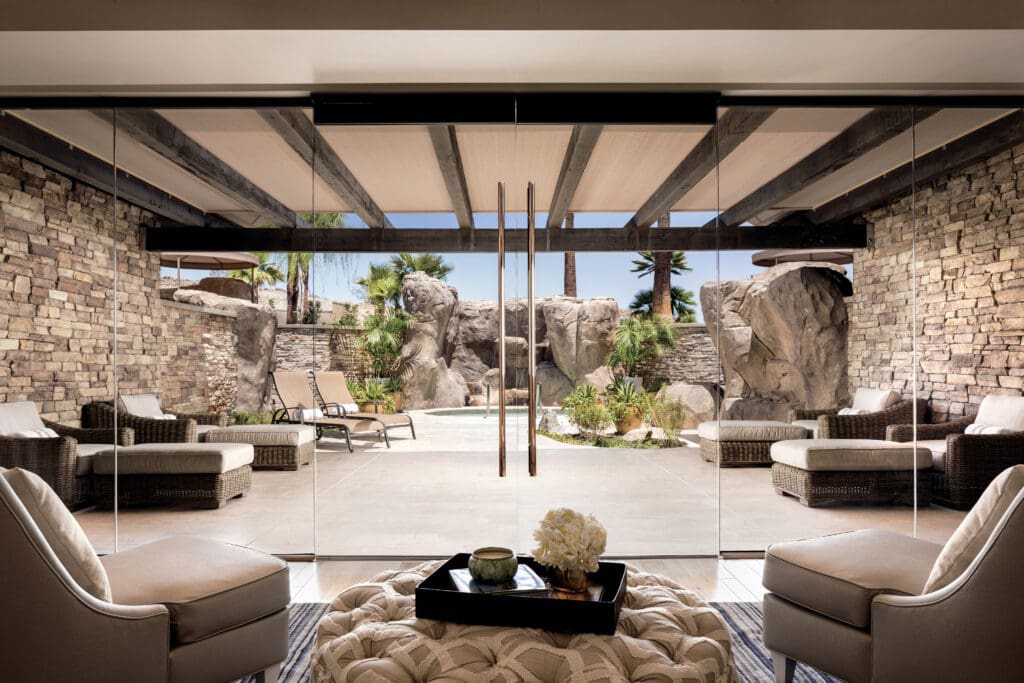 Elegant spa lounge at The Ritz-Carlton, Rancho Mirage featuring plush seating, glass doors, and a serene outdoor relaxation area with stone accents, palms, and desert-inspired landscaping.