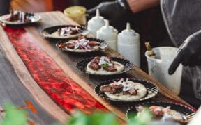 A row of plated tacos with meet and veggies with various squeeze sauces and a person pointing to them at Taste of AZ in Scottsdale.