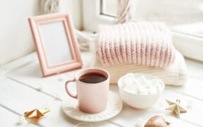 Valentine's Day trinkets, comfy knit blankets by the window, a frame and pink mug with marshmallow.