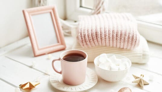 Valentine's Day trinkets, comfy knit blankets by the window, a frame and pink mug with marshmallow.