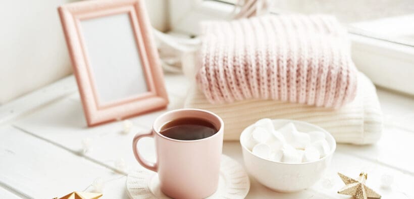 Valentine's Day trinkets, comfy knit blankets by the window, a frame and pink mug with marshmallow.