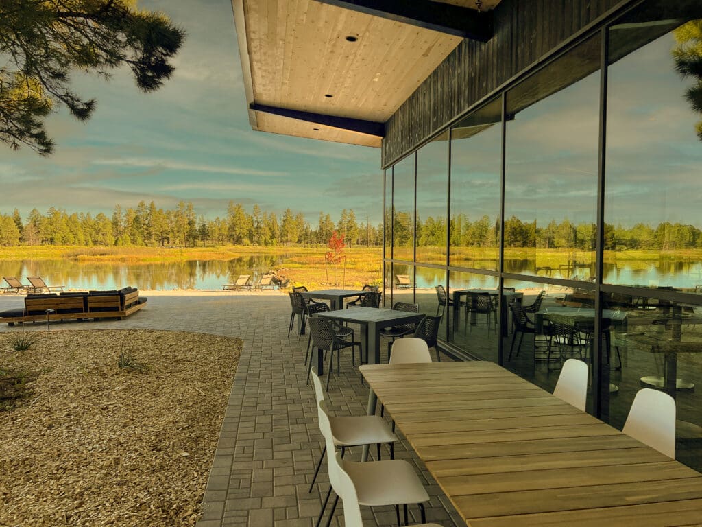 Outdoor patio at Backland Luxury Nature Resort with dining tables and lounge seating overlooking a small lake and pine forest near Williams, Arizona.
