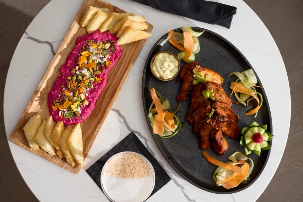 Plated après dishes at The Carter at Hotel Alpenrock, featuring chicken wings, vegetable garnishes, toasted bread and a vibrant beet dip.