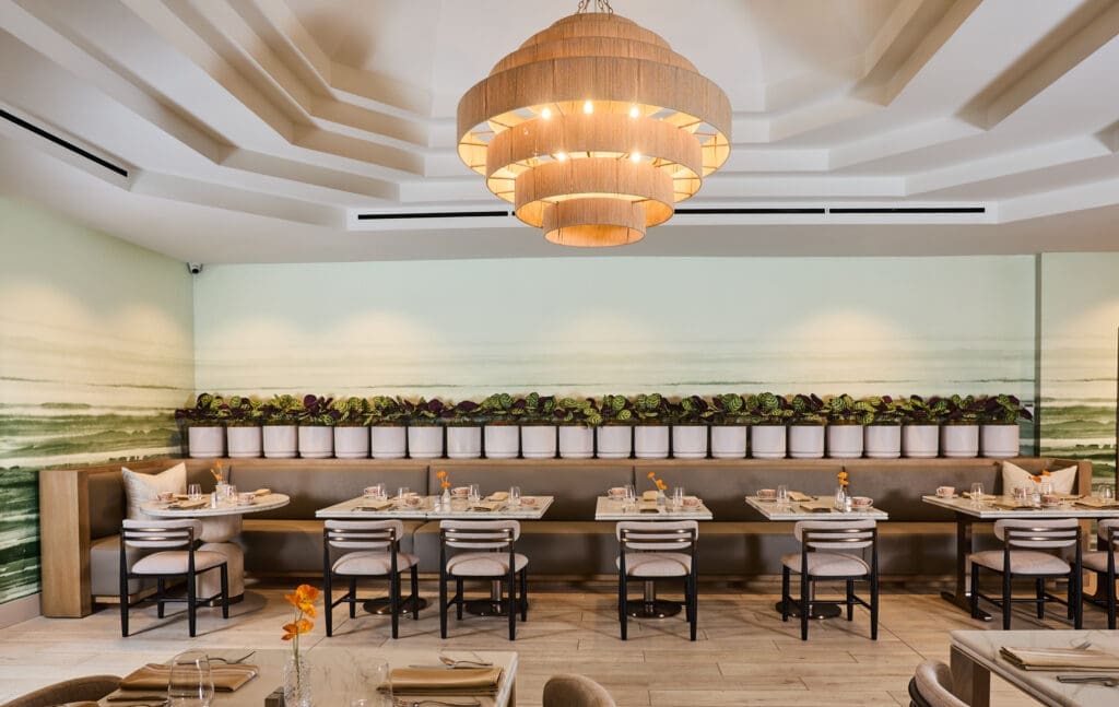 Interior of Poppy’s restaurant at Hilton Anaheim featuring modern seating, green mural walls and a large circular chandelier.